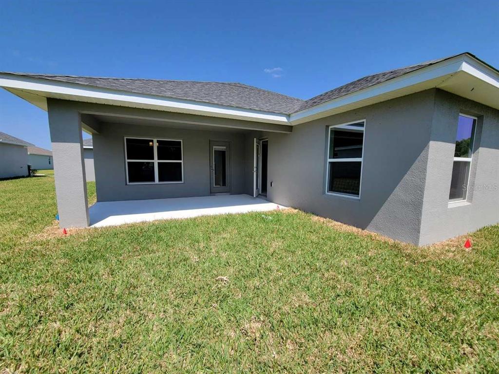 A gray stucco house features a covered concrete patio and a large grassy backyard — 4447 SW 91ST LANE ROAD, OCALA, FL