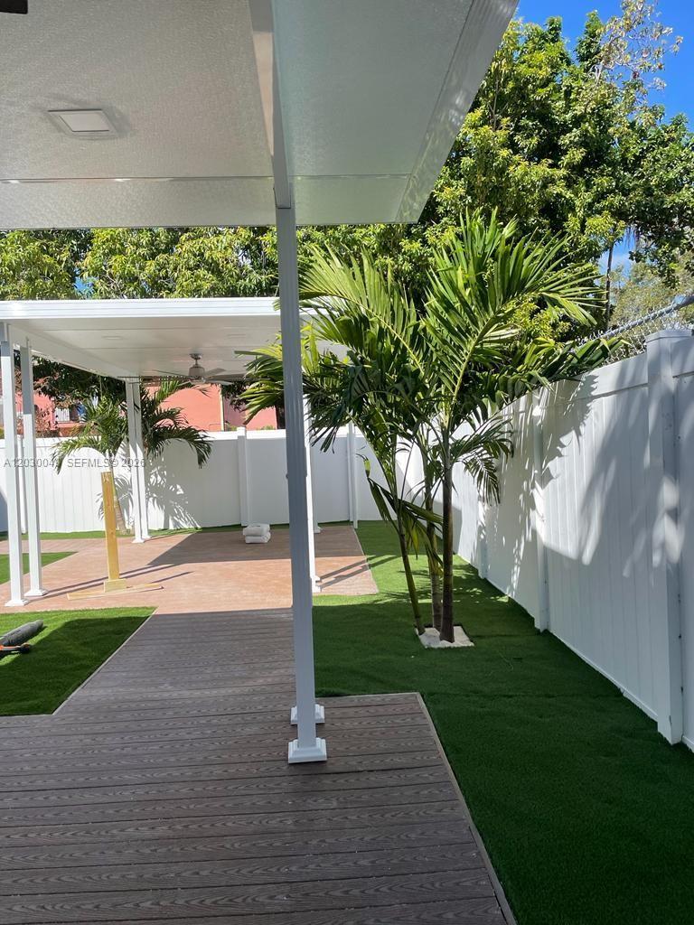 A covered patio with a wooden deck and artificial turf overlooks a fenced backyard — 331 SW 11th Ave, Miami FL 33130, MIAMI, FL