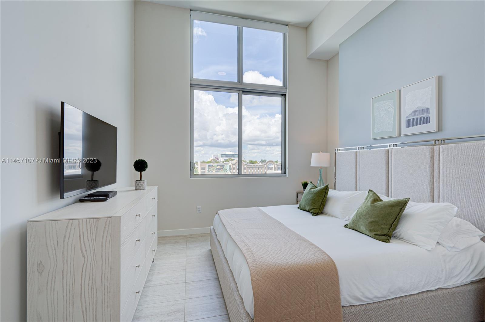 A bedroom features a bed with green pillows, a dresser with a television, and large windows — 3900 Biscayne Blvd # 502, Miami FL 33137, MIAMI, FL