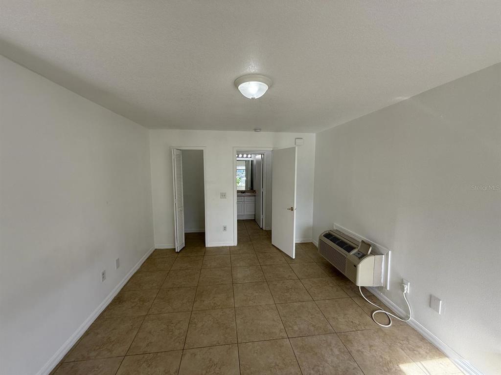 An empty room features beige tile flooring, white walls, a ceiling light, and a wall-mounted AC unit — 316 MANGO DRIVE UNIT B, DAVENPORT, FL
