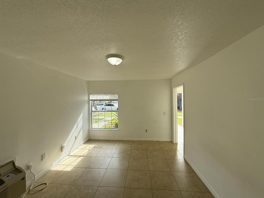 An empty room with beige tile flooring, white walls, a window, and a ceiling light — 316 MANGO DRIVE UNIT B, DAVENPORT, FL
