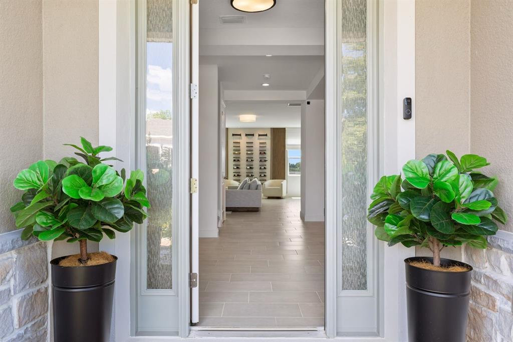 A front doorway with two potted plants leads into a bright, tiled home interior — 399 CHEEOTA COURT, MINNEOLA, FL