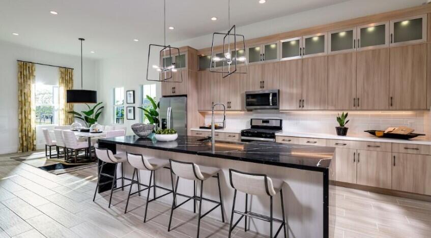 A modern kitchen features light wood cabinets, a black marble island, and a dining area — 9854 Regency Way, Palm Beach Gardens FL 33412, PALM BEACH GARDENS, FL