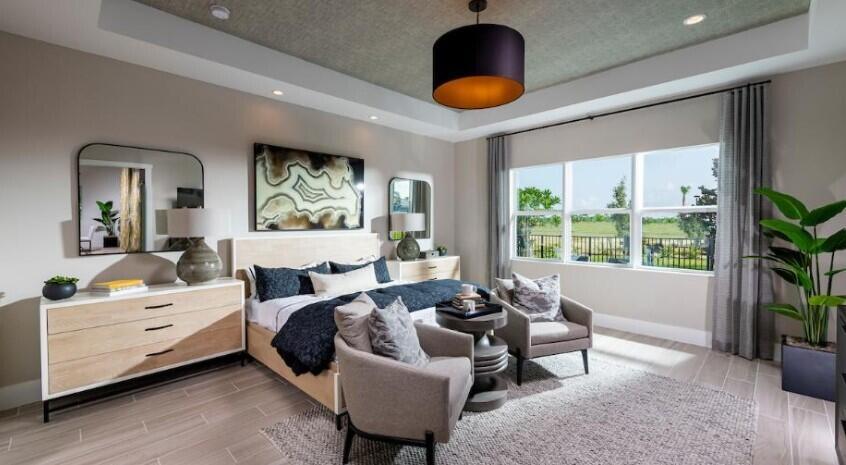 A modern bedroom features a tray ceiling, a bed with dark bedding, and two armchairs — 9854 Regency Way, Palm Beach Gardens FL 33412, PALM BEACH GARDENS, FL
