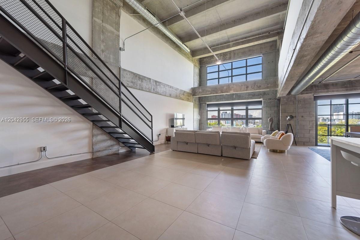 A spacious industrial-style living room features high concrete ceilings, a metal staircase, and large windows — 1749 NE Miami Ct # 507, Miami FL 33132, MIAMI, FL