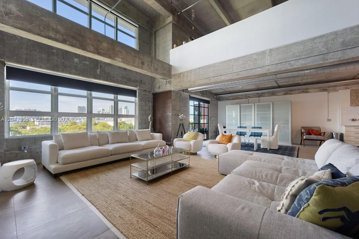 A spacious industrial-style living room features high concrete ceilings, large windows, and neutral furnishings — 1749 NE Miami Ct # 507, Miami FL 33132, MIAMI, FL