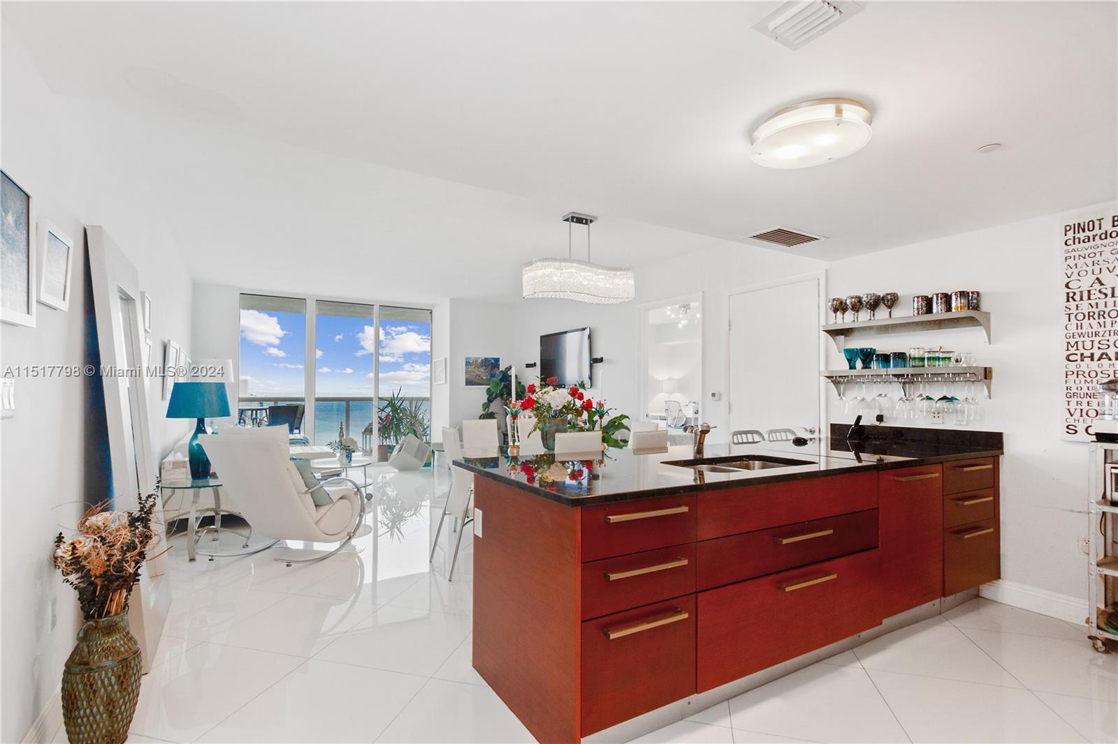 A modern kitchen with dark wood cabinets and a black countertop overlooks a bright living area — 1830 S Ocean Dr, Hallandale Beach FL 33009, HALLANDALE BEACH, FL