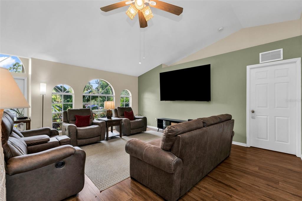 A living room features brown leather furniture, a wall-mounted television, and arched windows — 4413 S SAN MATEO DRIVE, NORTH PORT, FL