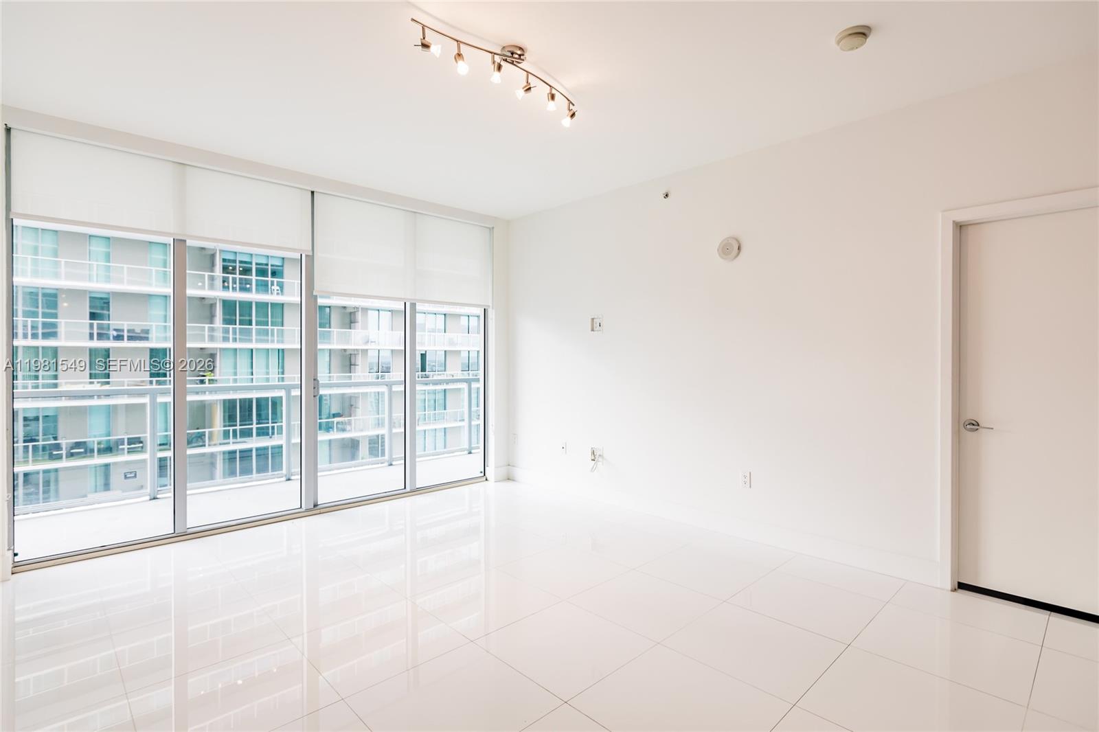A bright, empty room features white tile floors, a track light, and floor-to-ceiling windows — 1111 SW 1st Ave, Miami FL 33130, MIAMI, FL