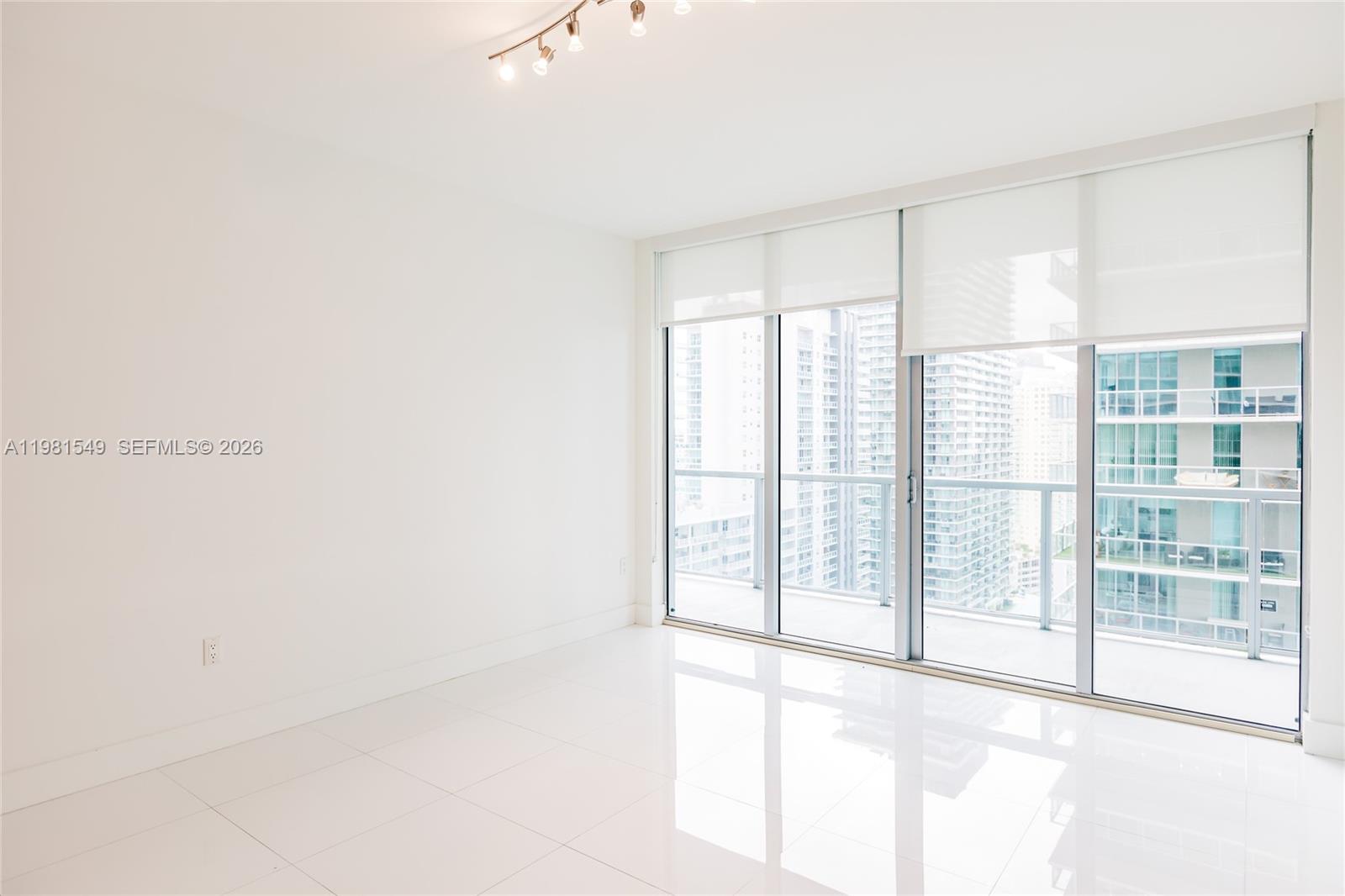 A bright, empty room features white tile floors, white walls, and floor-to-ceiling windows — 1111 SW 1st Ave, Miami FL 33130, MIAMI, FL
