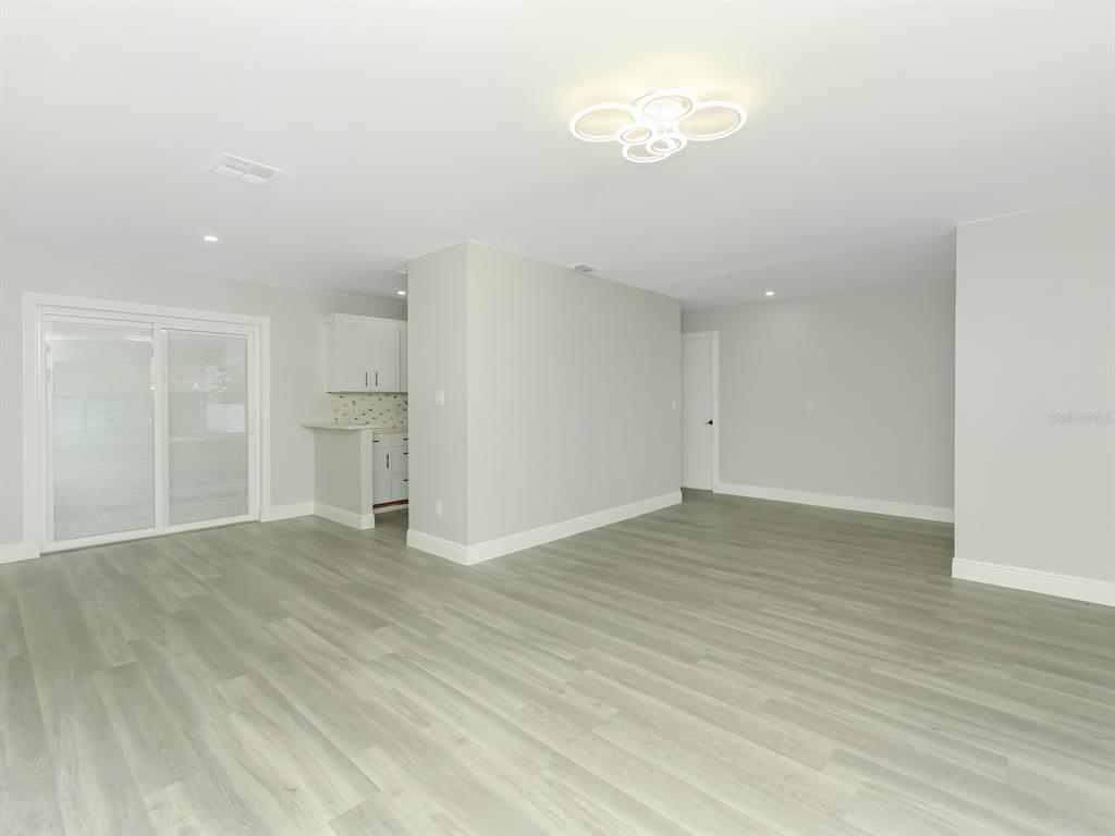 An open-concept living area features light gray wood-look flooring, white walls, and a modern light fixture — 919 SYLVIA DRIVE, DELTONA, FL