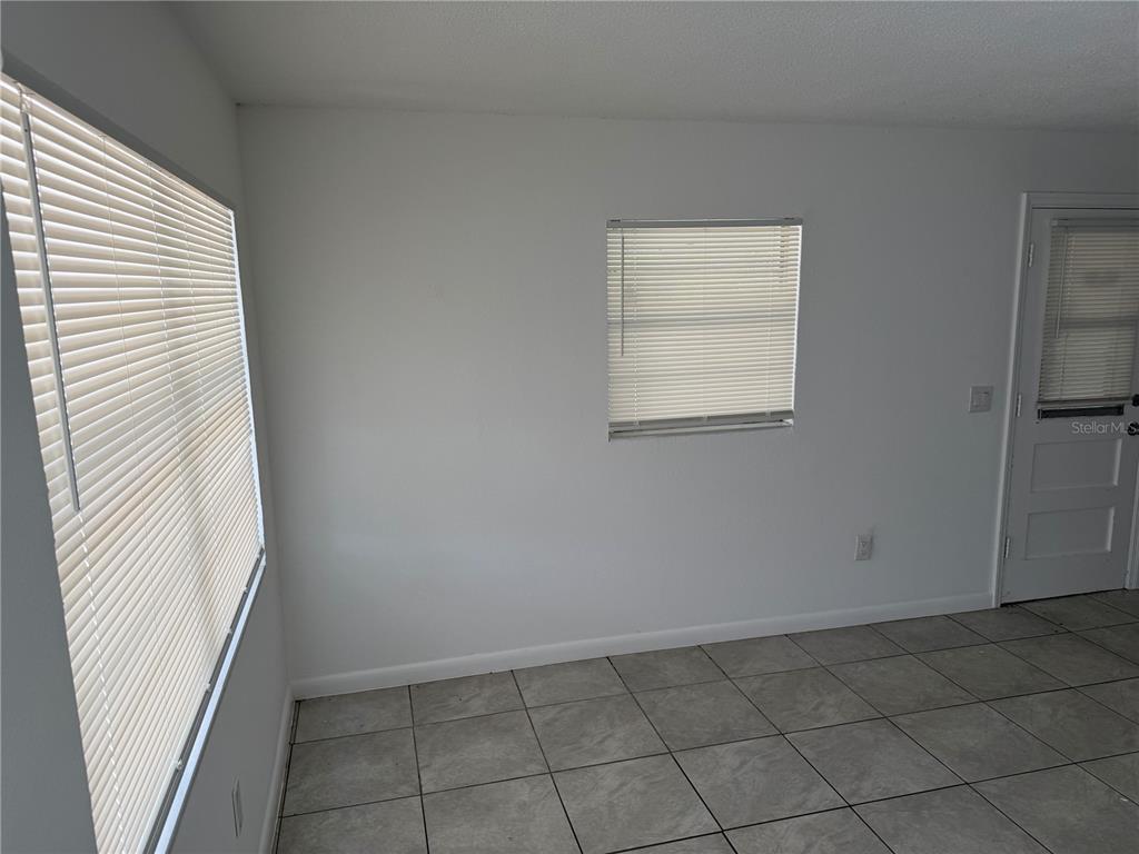 A room with white walls, tiled flooring, two windows with blinds, and a door — 1531 NE 14TH STREET, OKEECHOBEE, FL