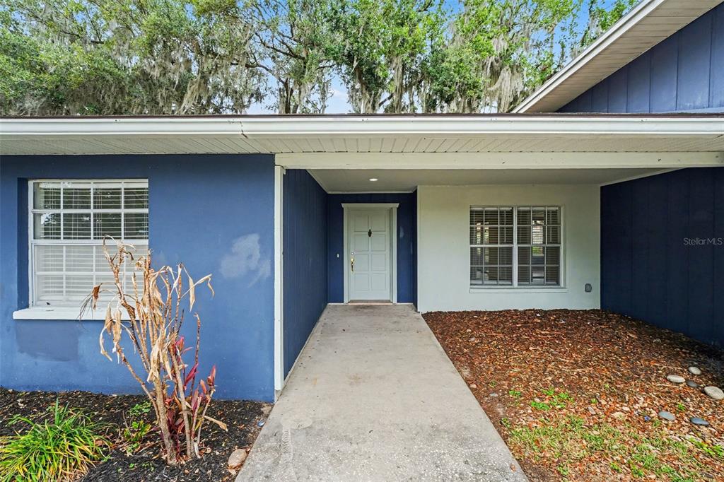A blue house exterior features a covered entryway, a light-colored door, and two windows — 1234 FAIRFAX N, LAKELAND, FL