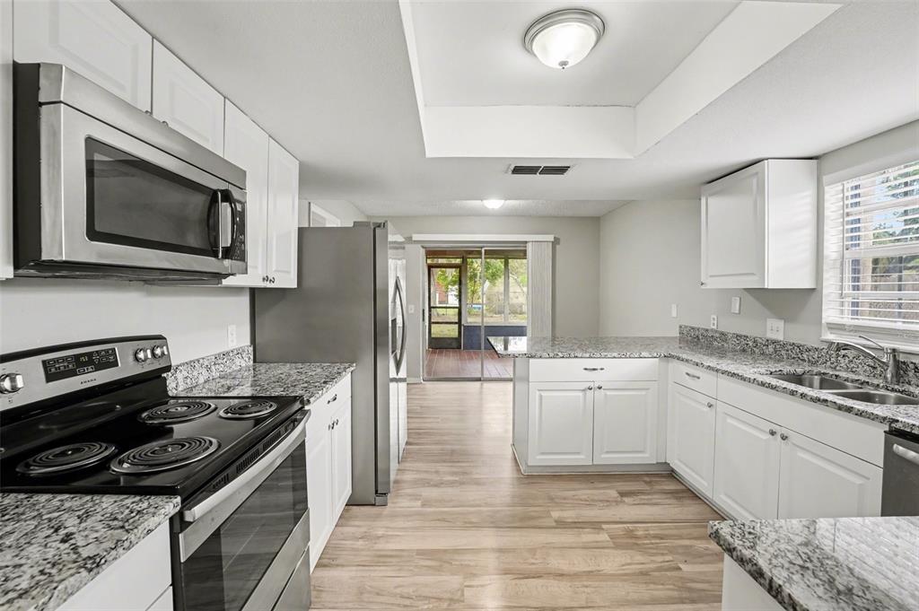A kitchen with white cabinets, granite countertops, stainless steel appliances, and wood-look flooring — 1234 FAIRFAX N, LAKELAND, FL