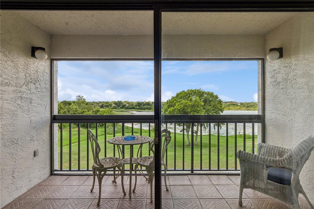 A covered balcony features tiled flooring, patio furniture, and a view of a lake — 1068 LOTUS PARKWAY UNIT 834, ALTAMONTE SPRINGS, FL