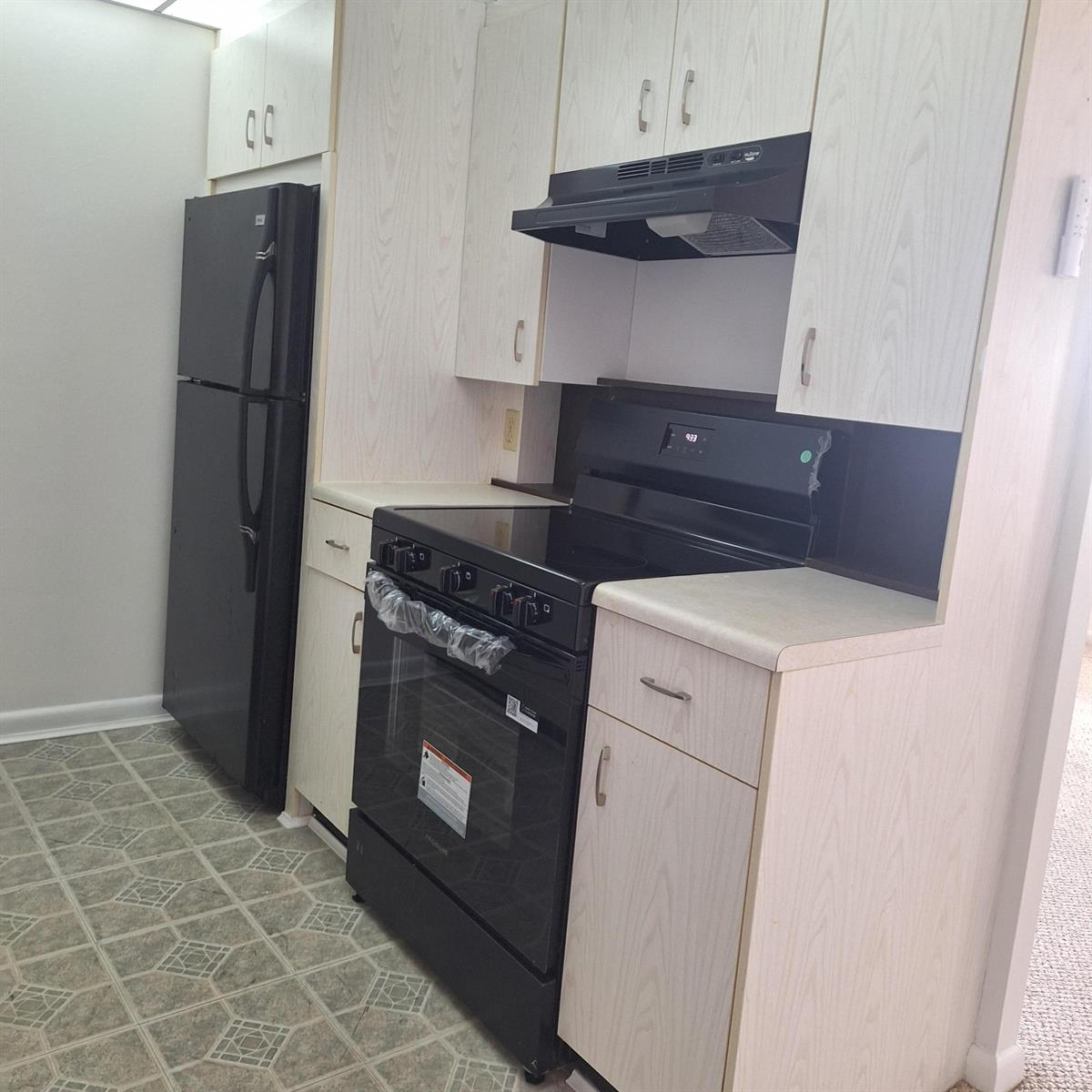 A kitchen features light wood cabinets, black appliances, and patterned vinyl flooring — 4007 Cornwall A # 4007, Boca Raton FL 33434, BOCA RATON, FL