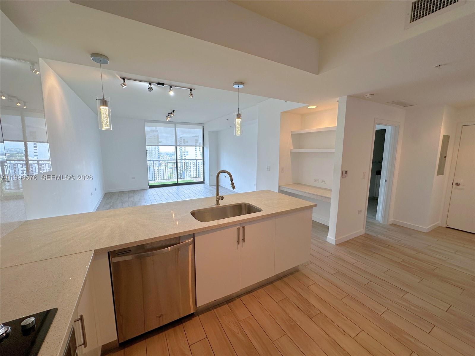 A modern kitchen with white cabinets, stone countertops, and light wood flooring overlooks a living area — 999 SW 1st Ave # 2109, Miami FL 33130, MIAMI, FL