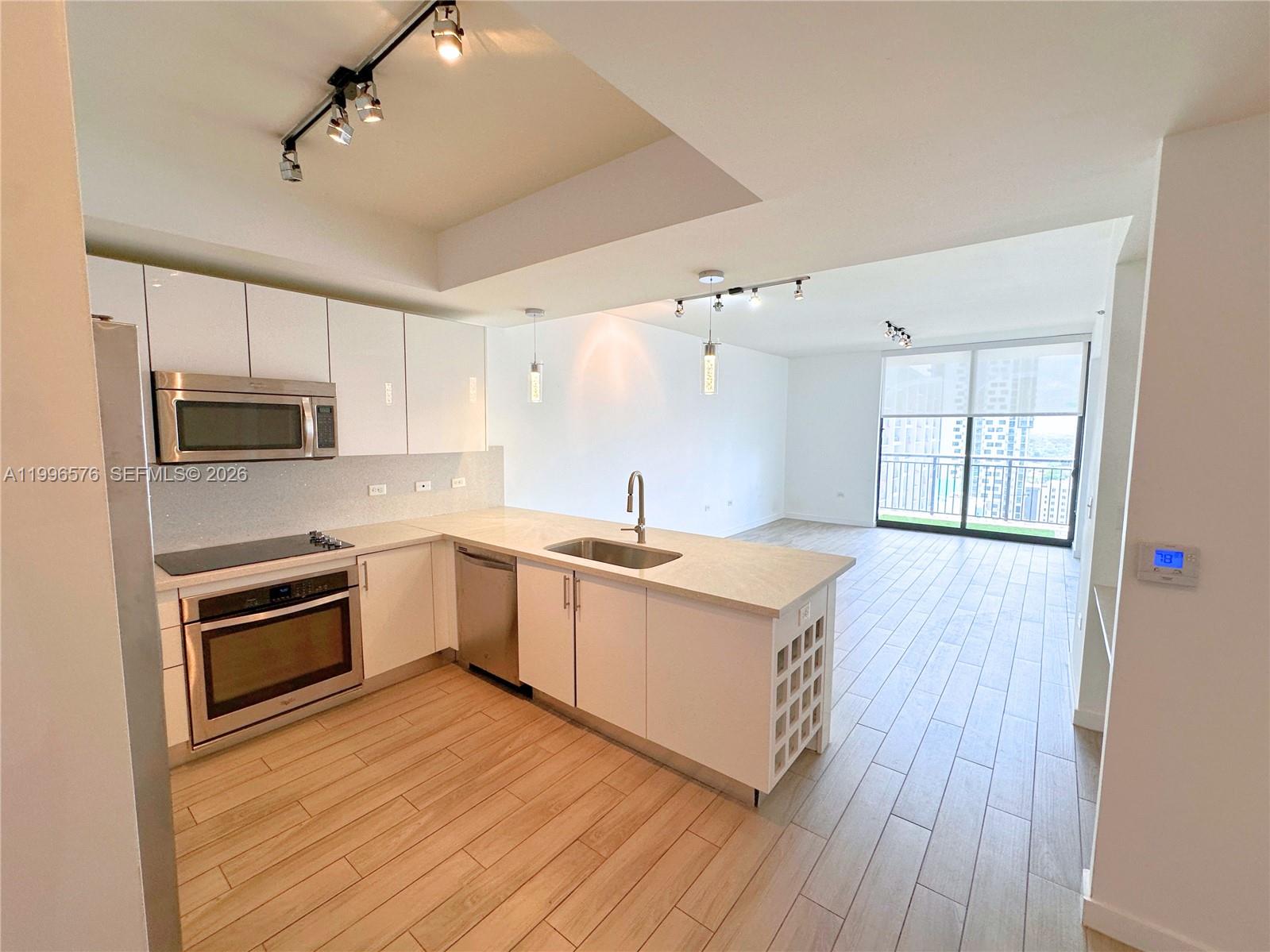 A modern kitchen with white cabinets and stainless steel appliances opens to a living area — 999 SW 1st Ave # 2109, Miami FL 33130, MIAMI, FL