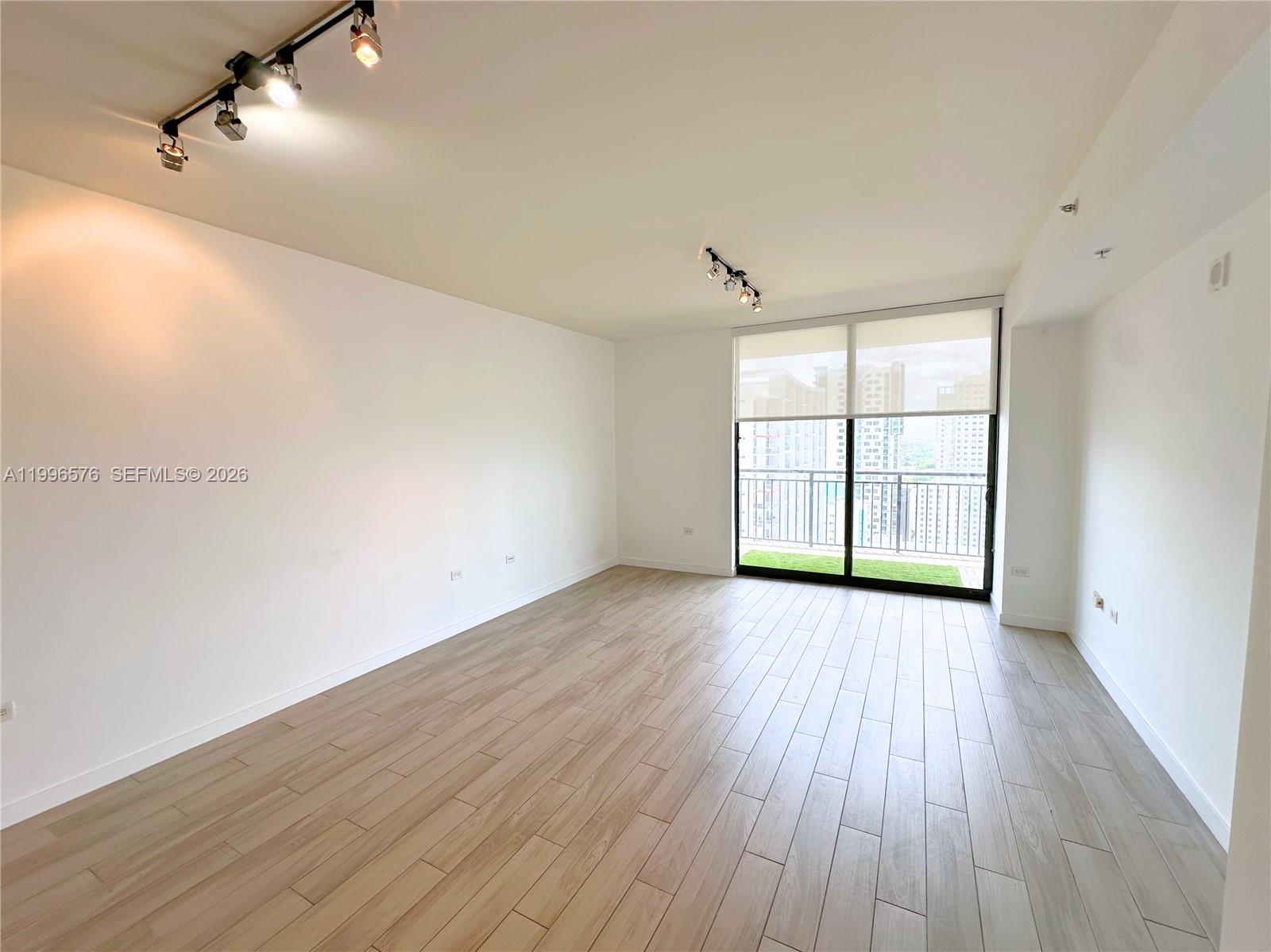 An empty living room features light wood-look tile flooring, white walls, and a balcony — 999 SW 1st Ave # 2109, Miami FL 33130, MIAMI, FL