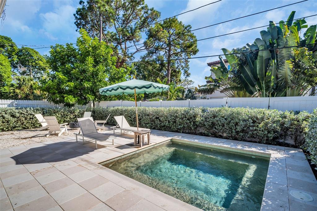 A small rectangular pool sits on a paved patio with lounge chairs and an umbrella — 218 49TH AVENUE N, ST PETERSBURG, FL
