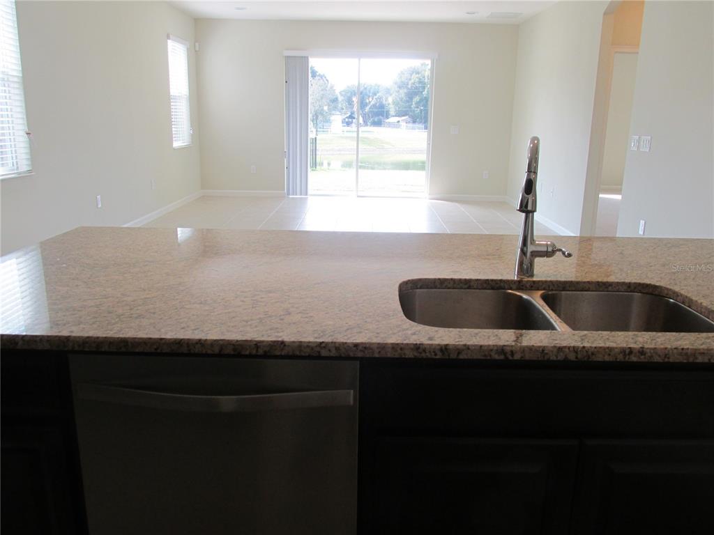 A kitchen island with a granite countertop and stainless steel sink overlooks an open living area — 2404 SABASTIAN STREET, MOUNT DORA, FL