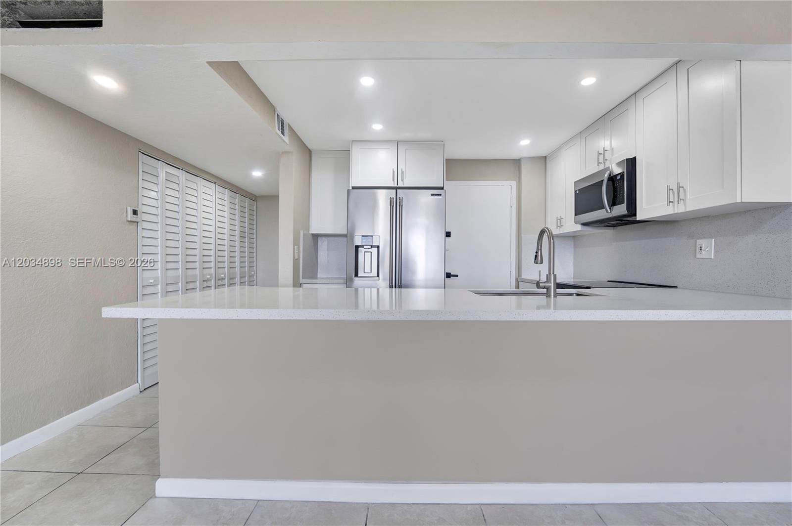 A kitchen features white cabinets, stainless steel appliances, and a white quartz breakfast bar — 9001 SW 77th Ave # C709, Miami FL 33156, MIAMI, FL