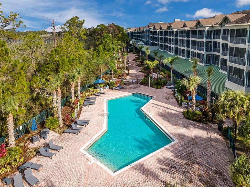 An aerial view shows a swimming pool on a brick patio beside a large building — 14200 AVALON ROAD UNIT 302, WINTER GARDEN, FL