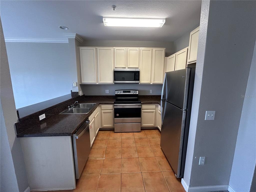 A kitchen features off-white cabinets, stainless steel appliances, dark countertops, and tiled flooring — 14200 AVALON ROAD UNIT 302, WINTER GARDEN, FL