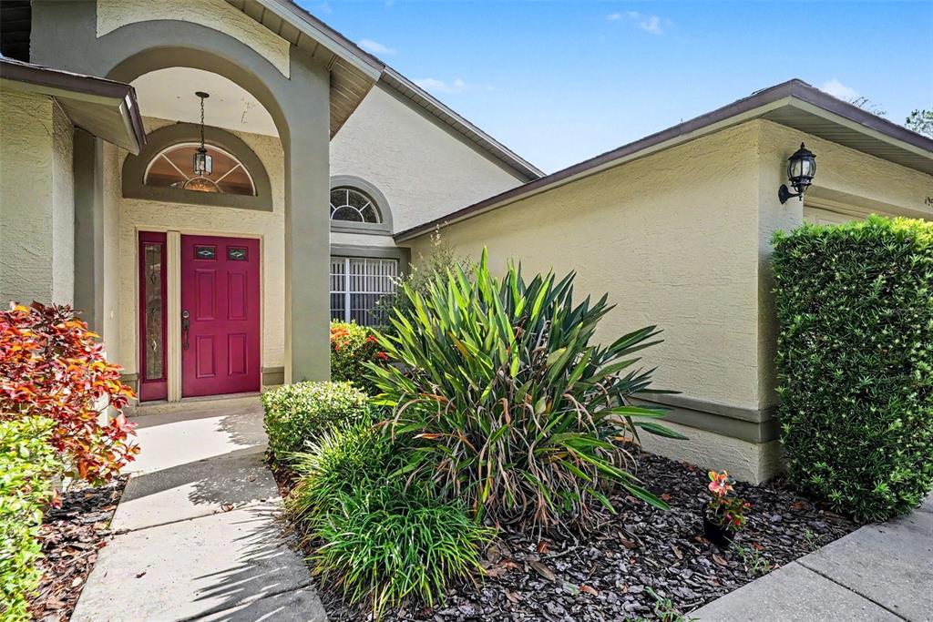 A front exterior view of a house with a red door and landscaped garden — 19610 WYNDMILL CIRCLE, ODESSA, FL
