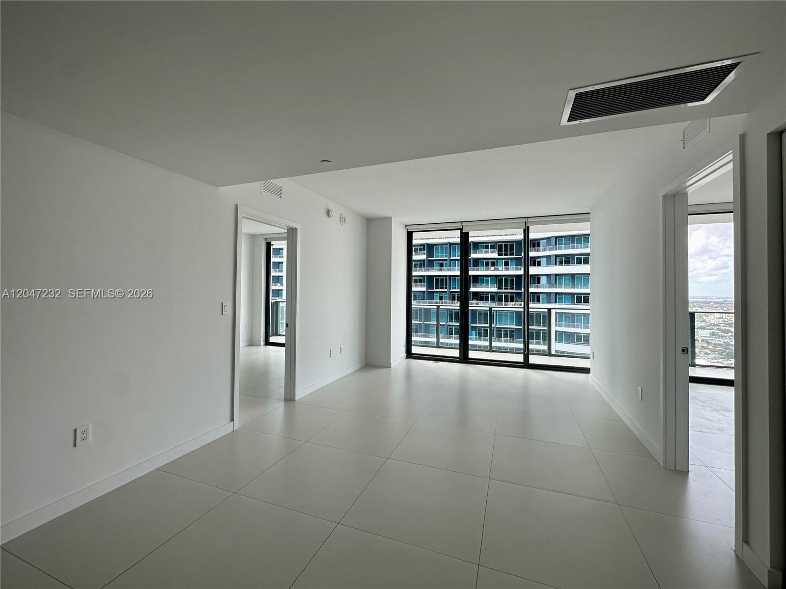 A bright, minimalist room features large floor-to-ceiling windows, white walls, and light-colored tile flooring — 1300 S Miami # 4209, Miami FL 33130, MIAMI, FL