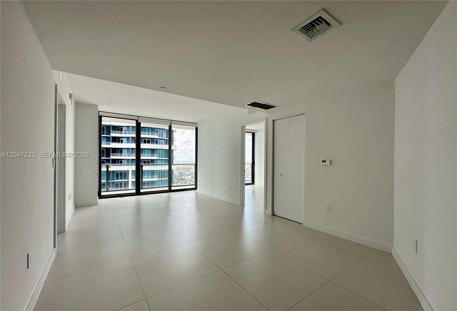 A bright, empty room with white walls, large floor-to-ceiling windows, and light-colored tile flooring — 1300 S Miami # 4209, Miami FL 33130, MIAMI, FL