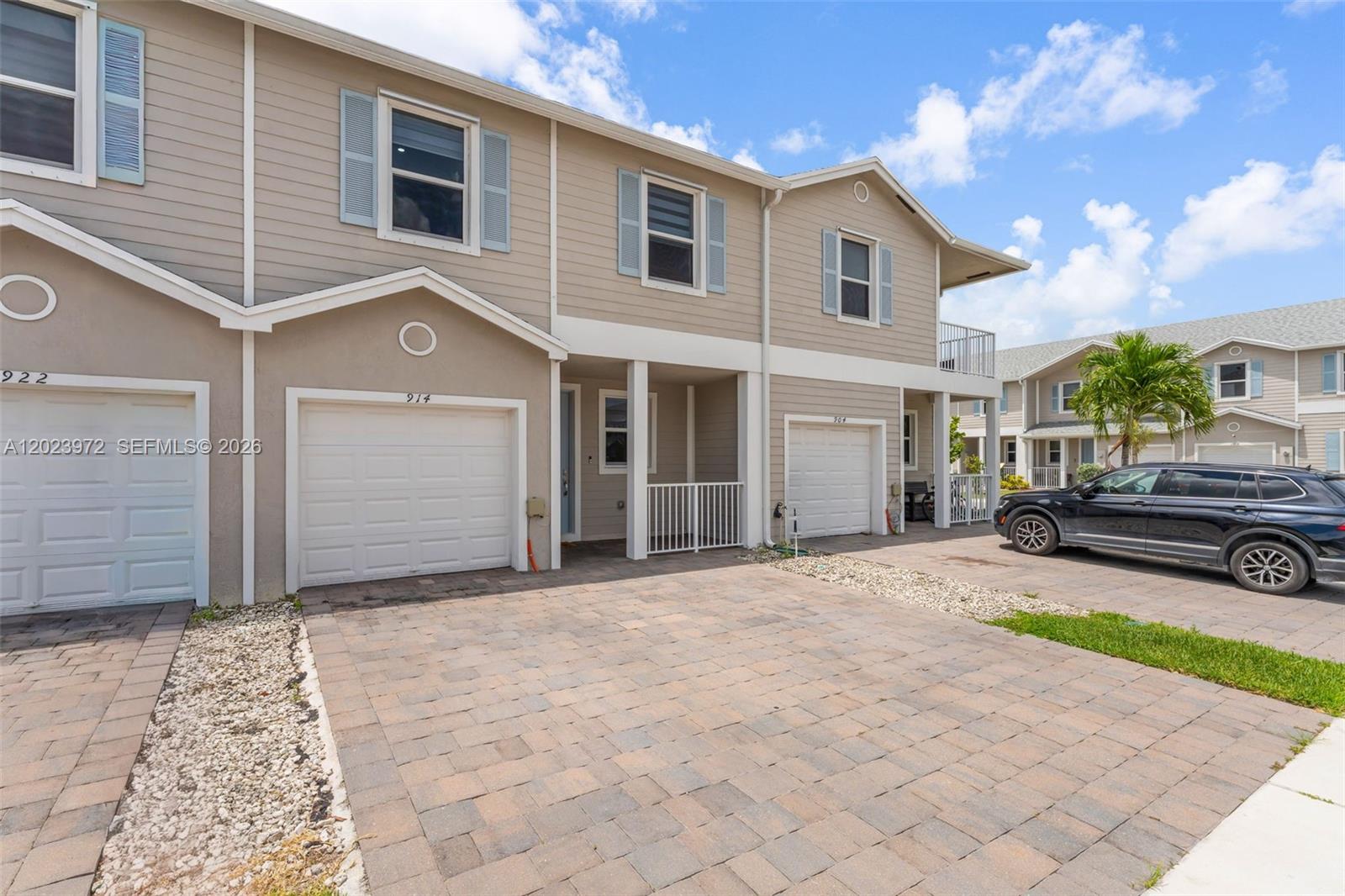 A two-story townhouse exterior features beige siding, a paved driveway, and a black SUV — 914 SE 18th St, Homestead FL 33034, HOMESTEAD, FL