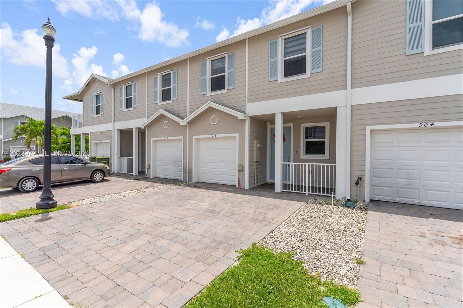 A row of two-story townhouses features beige siding, white garage doors, and paved driveways — 914 SE 18th St, Homestead FL 33034, HOMESTEAD, FL