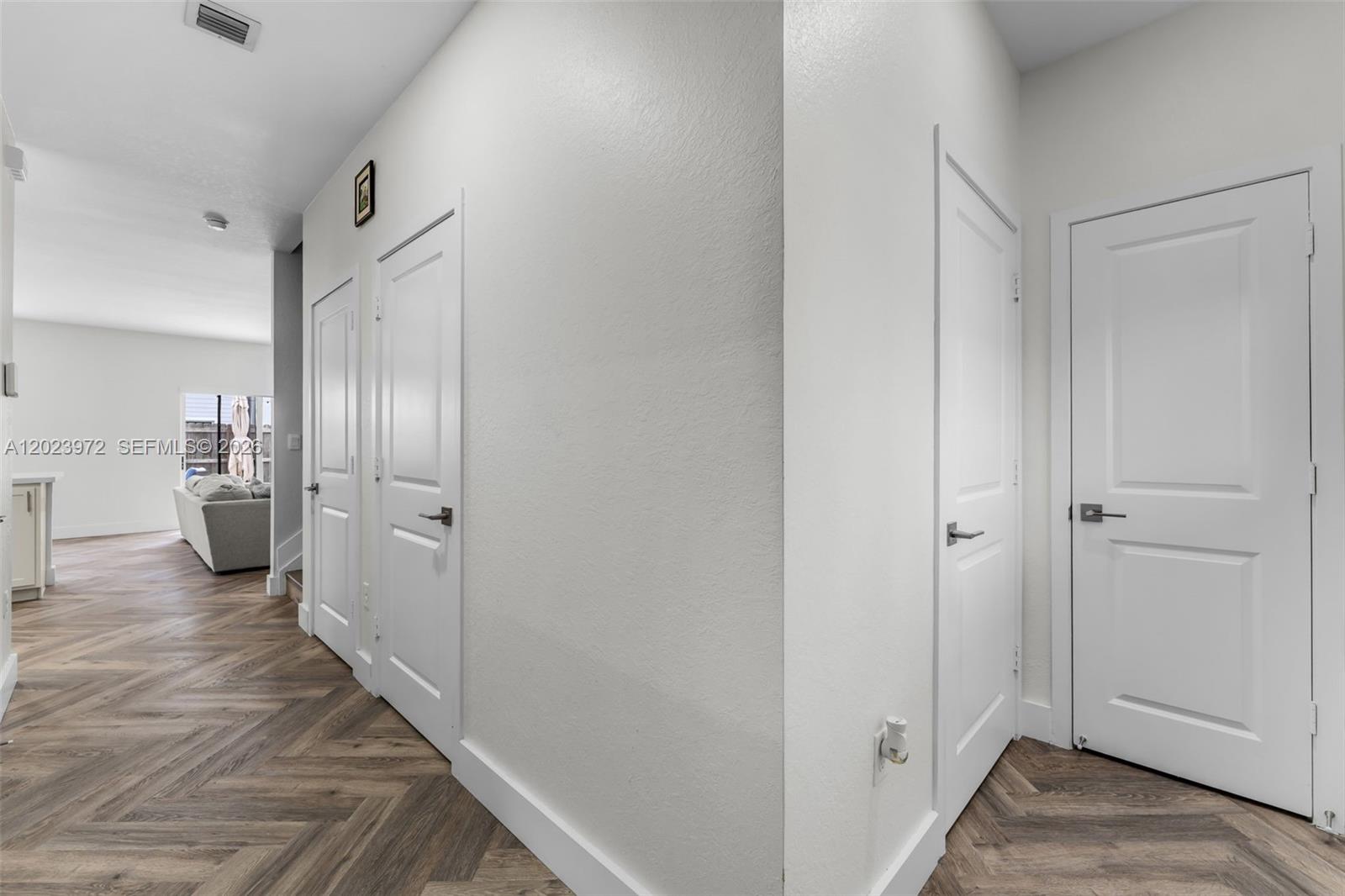 A hallway with white doors and herringbone-patterned wood flooring leads toward a living area — 914 SE 18th St, Homestead FL 33034, HOMESTEAD, FL