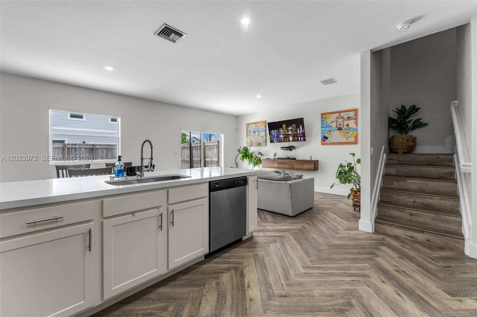 A kitchen island with a stainless steel dishwasher overlooks a living area with wood flooring — 914 SE 18th St, Homestead FL 33034, HOMESTEAD, FL