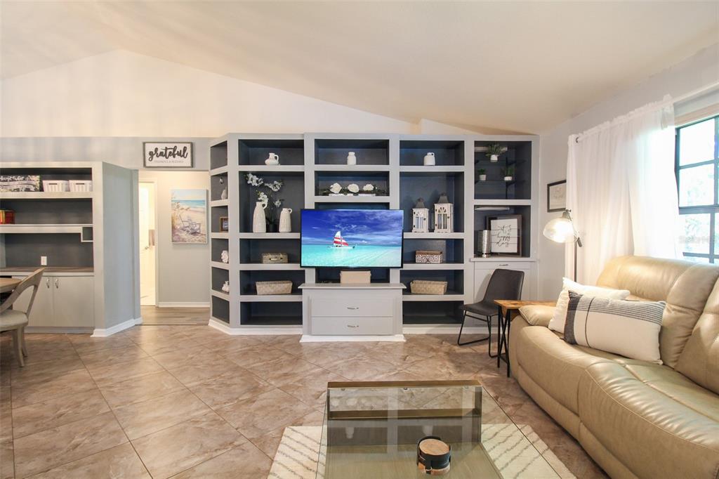 A living room features a large built-in shelving unit, a television, and tile flooring — 6029 22ND AVENUE CIRCLE E, PALMETTO, FL