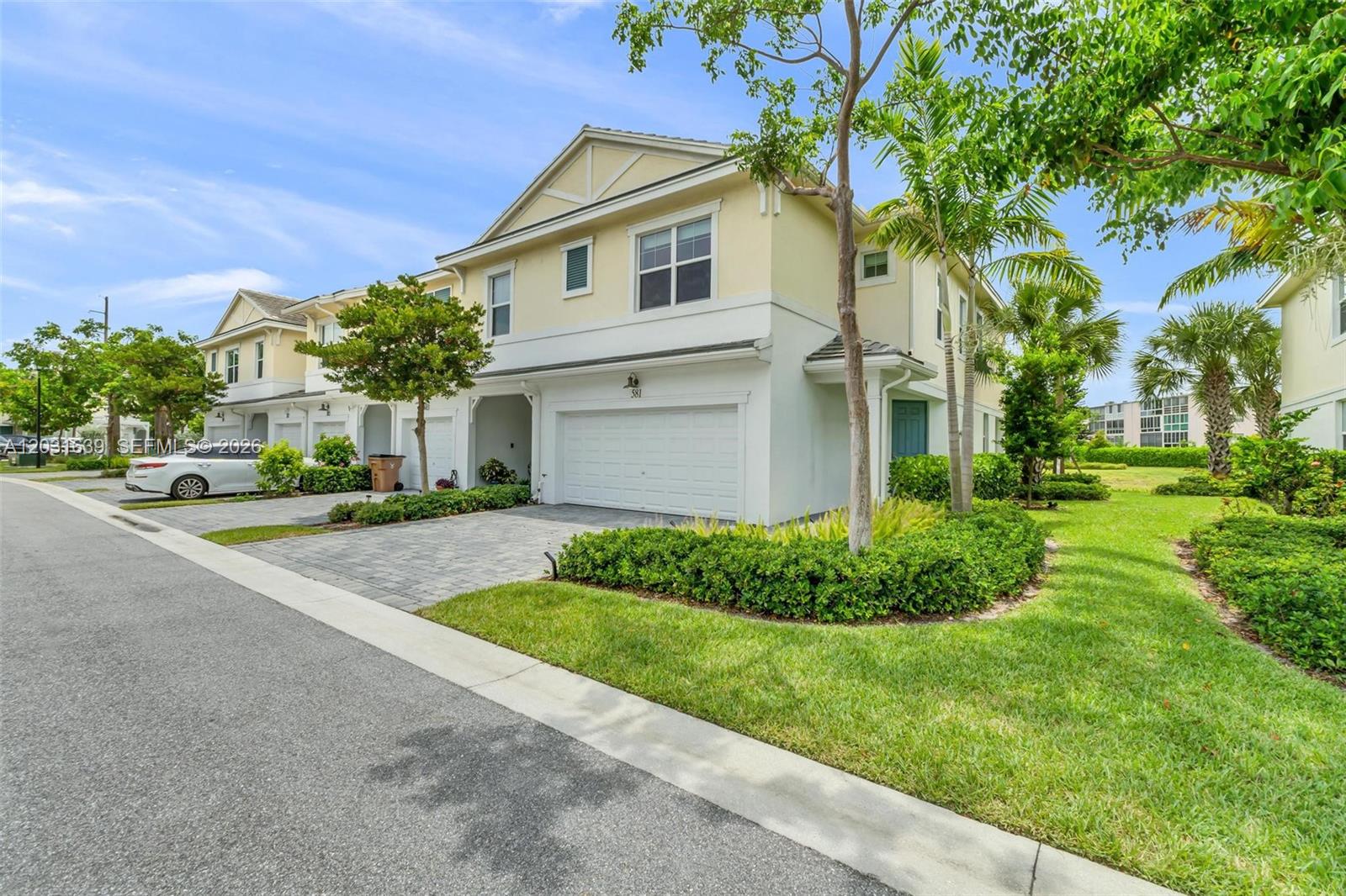 A two-story townhouse with a white garage, beige siding, and a paved driveway — 581 Sanderling Cir # 581, Deerfield Beach FL 33442, DEERFIELD BEACH, FL