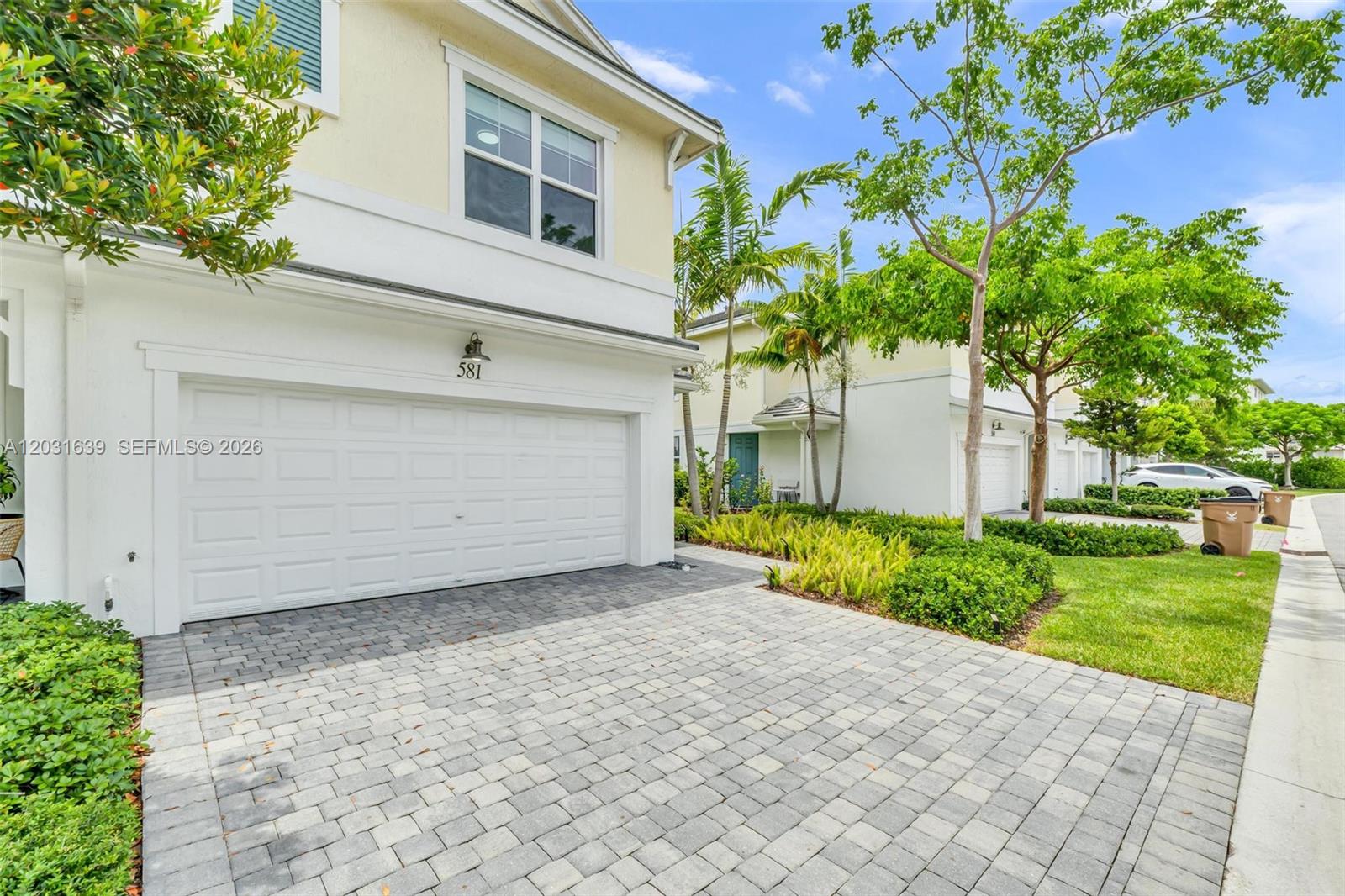 A two-story townhouse exterior features a white garage door, paved driveway, and palm trees — 581 Sanderling Cir # 581, Deerfield Beach FL 33442, DEERFIELD BEACH, FL