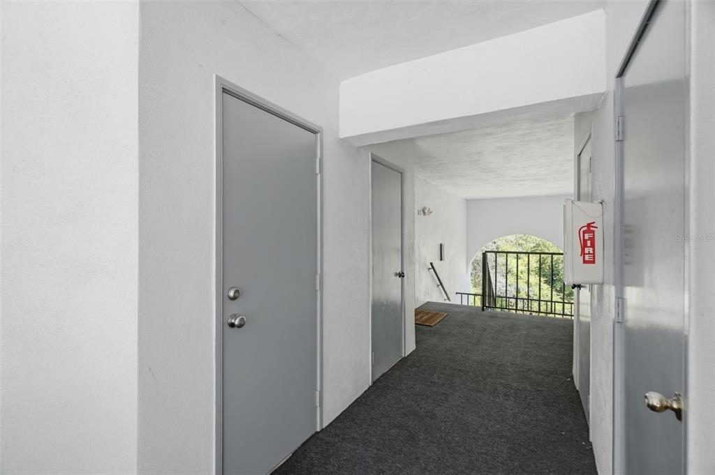 A hallway with grey doors, carpeted flooring, and a wall-mounted fire extinguisher cabinet — 1182 PINE RIDGE CIRCLE W UNIT A3, TARPON SPRINGS, FL