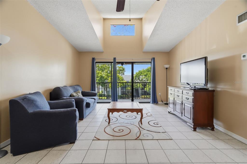A living room features a vaulted ceiling, tile flooring, a sofa, and a sliding glass door — 1182 PINE RIDGE CIRCLE W UNIT A3, TARPON SPRINGS, FL