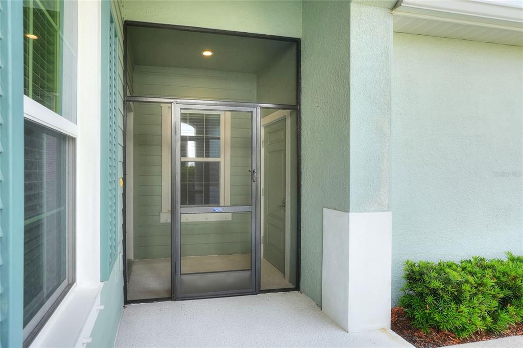 A covered entryway features a screen door, light green siding, and a concrete porch floor — 13531 CIRCA CROSSING DRIVE, LITHIA, FL