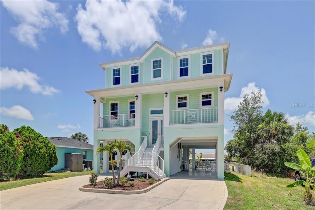 A three-story, light green elevated house with a white staircase and a concrete driveway — 4389 5TH ISLE DRIVE, HERNANDO BEACH, FL