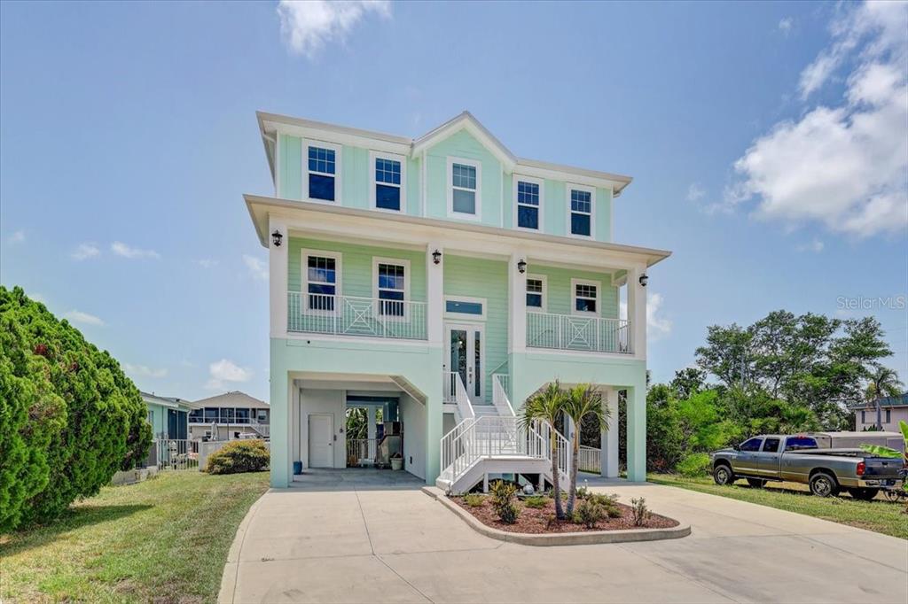 A light green, three-story elevated house with a concrete driveway and a front staircase — 4389 5TH ISLE DRIVE, HERNANDO BEACH, FL