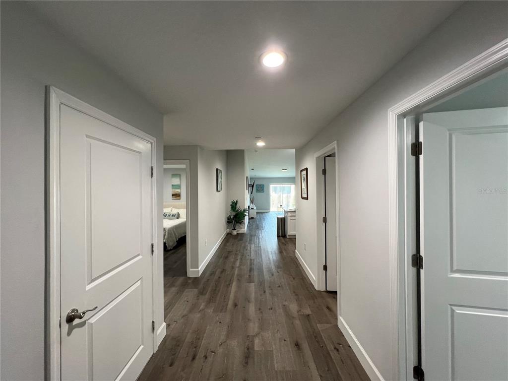 A hallway with wood-look flooring leads toward an open living area and sliding glass doors — 9092 AGATE STREET, PORT CHARLOTTE, FL