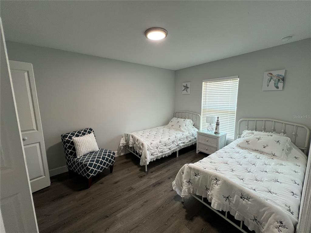 A bedroom features two twin beds, a patterned armchair, and wood-look flooring — 9092 AGATE STREET, PORT CHARLOTTE, FL