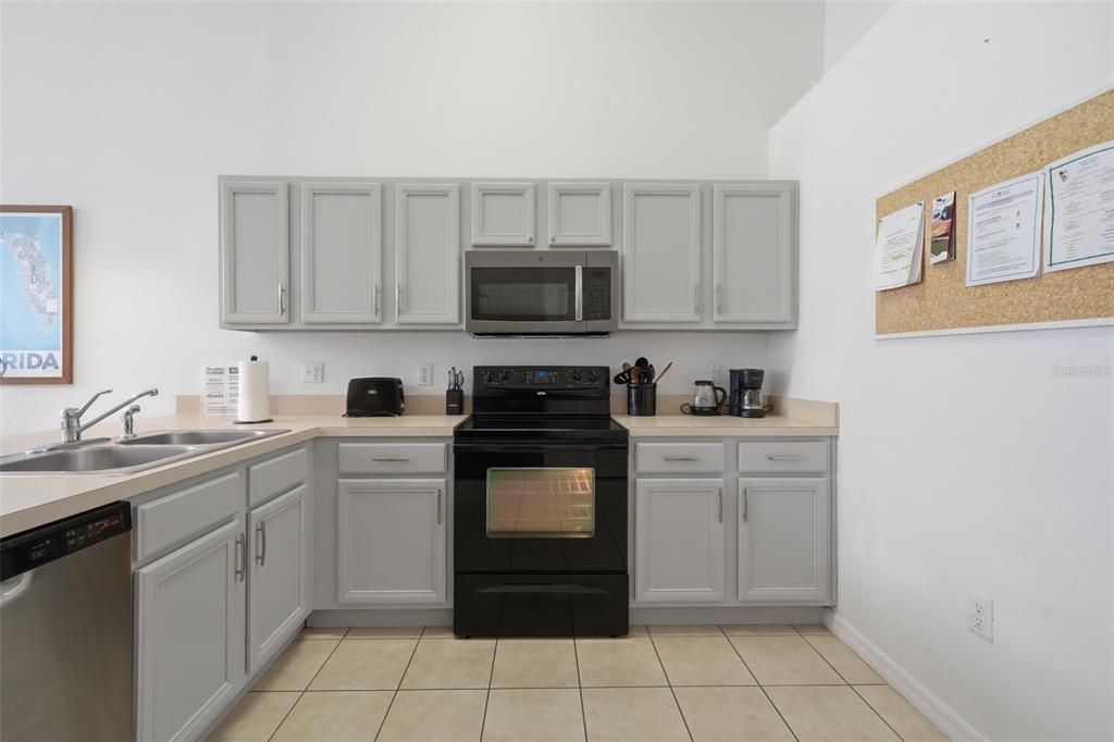 A kitchen features gray cabinets, black appliances, a double sink, and beige tile flooring — 155 BAREFOOT BEACH WAY, KISSIMMEE, FL