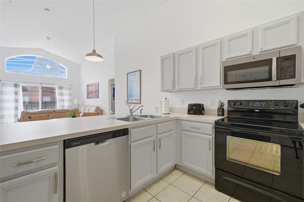 A kitchen with light gray cabinets, stainless steel appliances, and a view into the living area — 155 BAREFOOT BEACH WAY, KISSIMMEE, FL