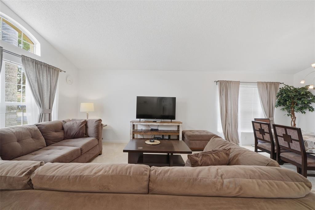 A living room features a large brown sectional sofa, a television on a wooden stand, and dining furniture — 155 BAREFOOT BEACH WAY, KISSIMMEE, FL