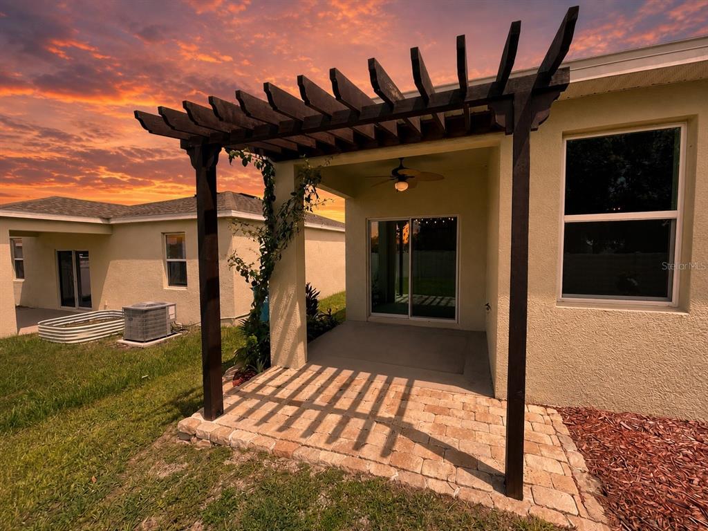 A patio with a wooden pergola and stone pavers sits outside a house at sunset — 689 CROWN ROSE DRIVE, EAGLE LAKE, FL