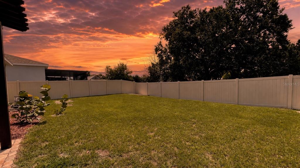A grassy backyard features a white vinyl fence and a large tree at sunset — 689 CROWN ROSE DRIVE, EAGLE LAKE, FL
